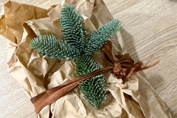 A creatively wrapped gift featuring eco-friendly brown paper and a decorative pine sprig, tied with a brown ribbon. emphasizes sustainable and natural themes trending in gift wrapping.