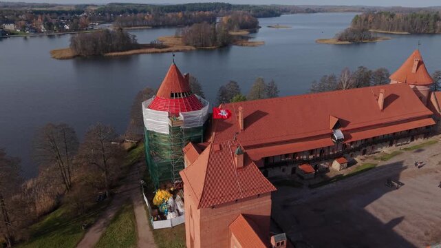 Trakai Island Castle Traku Pilis In Lithuania Close Aerial Approach To Trakai Waterfront Fortress With Red Tiled Roofs And Scaffolded Tower, Islets And Calm Lake In Background Lively