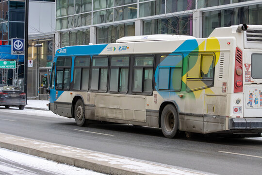 Canada, Montreal, 22 December 2025 : City bus passes snowy street near metro entrance colorful buildings