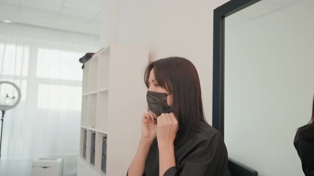 caucasian hairdresser in salon putting mask, preparing for client appointment, adjusting black protective mask in front of mirror, soft natural light, ringlight visible, calm focused expression, sleek