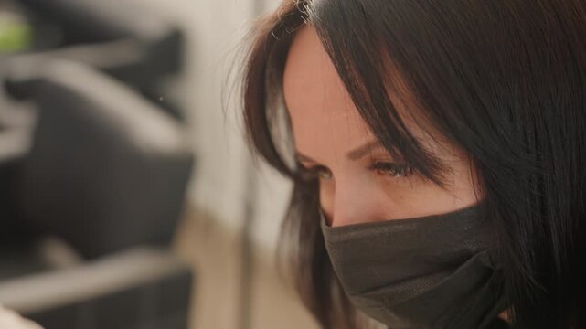 closeup salon microblading session female technician focused on precise eyebrow shaping, black mask, dark hair, indoor studio setting, sterile tools, client hand visible, warm ambient lighting, calm