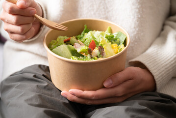 Healthy vegetable salad in takeout bowl holding by woman hand and eating