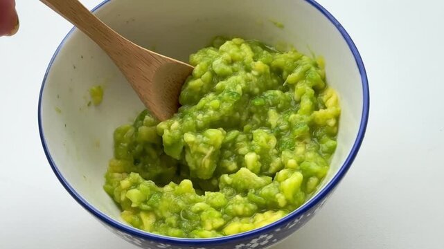 Stirring mashed avocado in the bowl with a spoon.