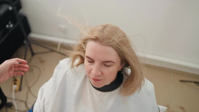 blonde caucasian woman smiling after haircut stylist hand visible as cape drapes, soft natural light and gentle movement highlight fresh bob and polished ends, candid closeup portrait showing