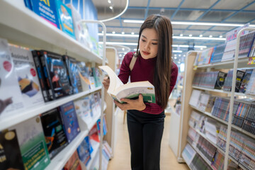 Asian woman reading book in modern bookstore