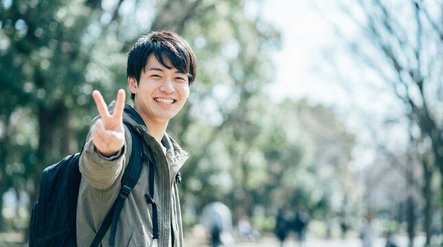 公園でピースサインを出す笑顔の日本人男子大学生