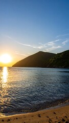 A scenic coastal view capturing a sunlit ocean horizon, with a mountain range shadowed against a vibrant blue sky