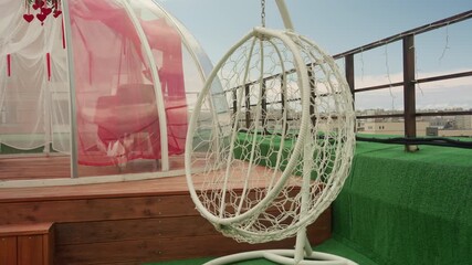 rooftop terrace with hanging chair, glass dome with pink interior, wooden deck, green turf, metal railing and urban skyline view intimate modern lounge set for romantic staycation or quiet retreat