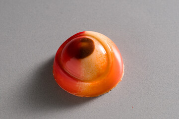 Single luxury handmade chocolate bonbon with red and orange glossy shell on a grey background