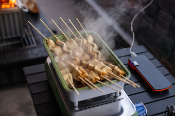 Steaming Korean fish cake skewers (Eomuk) boiling in a rectangular pot, winter outdoor camping vibes, warm broth, steam rising, delicious street food style.