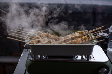 Steaming Korean fish cake skewers (Eomuk) boiling in a rectangular pot, winter outdoor camping vibes, warm broth, steam rising, delicious street food style.