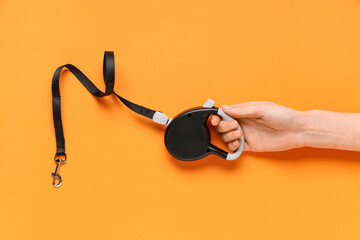 Female hand with black retractable dog leash and lead on orange background