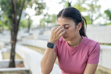 Asian women in sportswear touching her forehead with closed eyes, showing signs of headache, fatigue or stress during outdoor activity, concept of health awareness and mental strain.