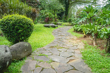 Obraz premium Stone pathway winding through a lush green garden, creating a peaceful atmosphere for walking, relaxation, and connection with nature in an outdoor park setting.