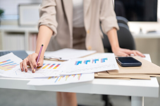 Close up of a businesswoman or office worker's hand holding a pencil over documents with graph chart