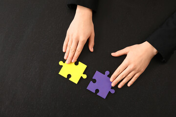 Female mediator's hands with puzzle pieces on black table, top view