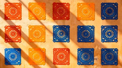 Colorful papel picado displayed on wall with shadows during daylight in a traditional setting