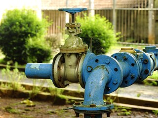 Fototapeta premium Close-up of an industrial blue gate valve and piping system outdoors. This weathered water infrastructure shows signs of moss and age, representing utility management and engineering.