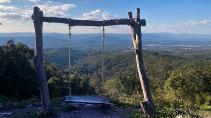 Rustic wooden swing overlooking a vast green mountain landscape under blue sky, scenic viewpoint symbolizing freedom, travel, relaxation and connection with nature.