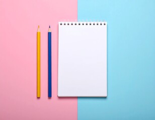 A flat lay photograph with a blank white spiral notebook and two colored pencils (yellow & blue) on a split pink and blue background