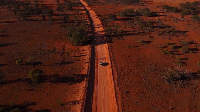 Drone following a straight dirt track car racing down stretching across red outback plains toward distant horizon, Australian wilderness