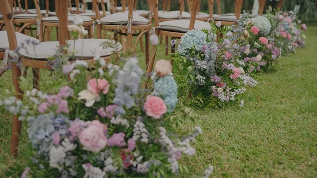 Wedding aisle chairs lined with pastel flowers arranged on grass