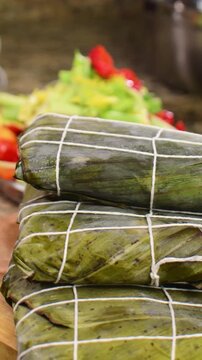 pile of freshly assembled hallacas spinning, traditional Venezuelan Christmas dish, expertly wrapped in smoked banana leaves and secured with white twine in a classic grid pattern.