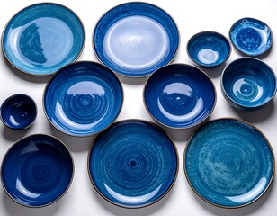 A flat lay showcases a collection of varied blue ceramic plates and bowls with subtle marbling and a golden trim against a white backdrop