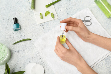 Female hands holding bottle of cuticle oil with towel, aloe vera and scissors on light grunge...