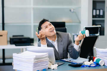 Exhausted businessman holding coffee cup at desk, feeling tired and overworked with paperwork and deadlines in modern office environment.