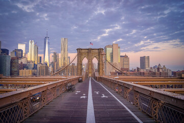 Obraz premium Brooklyn Bridge pedestrian walkway facing Lower Manhattan at golden hour sunset, vital NYC link for pedestrians and global commerce, United States of America. 