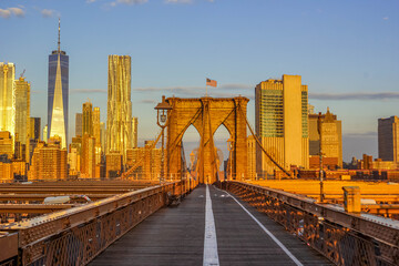 Obraz premium Brooklyn Bridge pedestrian path toward Lower Manhattan skyline at sunrise, iconic NYC crossing for commuters and tourists, United States of America. 