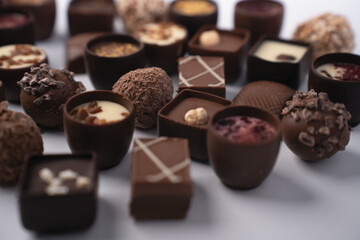 close-up of assorted gourmet chocolate pralines and truffles arranged on a white surface; shallow depth-of-field highlights rich brown and cream tones, textured toppings, glossy shells and artisanal e
