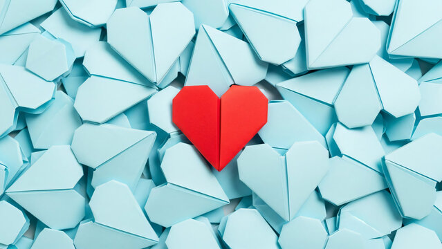 A single vibrant red origami heart stands out from a background of light blue paper hearts, symbolizing uniqueness, individuality, and love