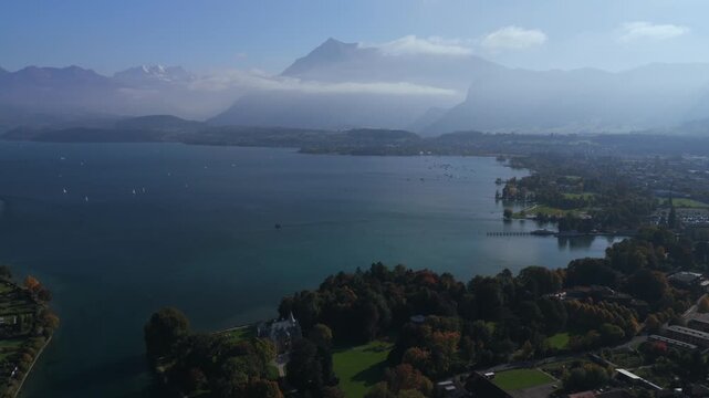 Thunersee Lake Thun Flusswelle Aare River aerial drone Thun Switzerland Schweiz Swiss Alps Fall Autumn sunny morning low clouds haze Bernese Oberland Interlaken boats Schloss Schadau circle right