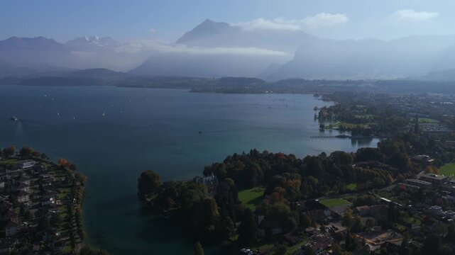 Thunersee Lake Thun Flusswelle Aare River aerial drone Thun Switzerland Schweiz Swiss Alps Fall Autumn sunny morning low clouds haze Bernese Oberland Interlaken still water boats forward pan up motion