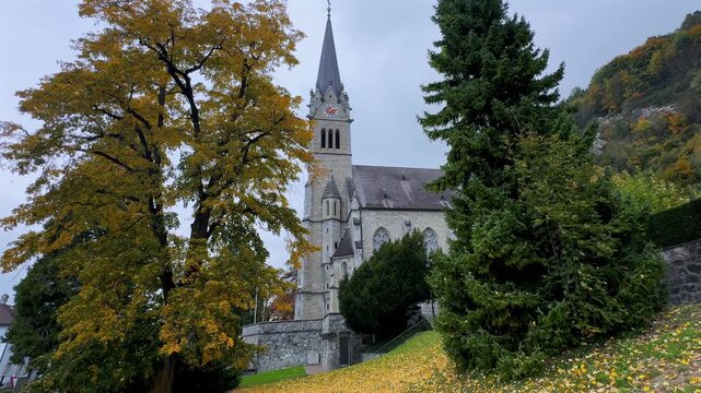 Fall Autumn morning Cathedral Chapel Katherdrale St Florin Neo gothic building parish church Vaduz Liechtenstein Lichtenstein windy falling golden leaves Larch Tree cloudy grey skies October November