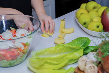 Hands slicing an apple on a white counter next to a large bowl of fresh salad, promoting healthy lifestyle