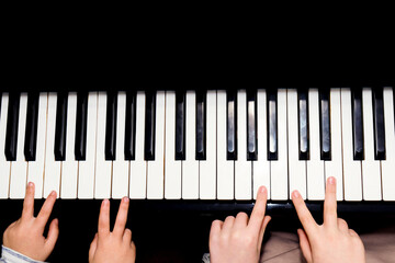 Children's hands learning to play music on a piano keyboard, showing concentration and the educational process