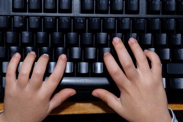 Child's small hands learning to type on a dark computer keyboard, highlighting early education and digital literacy