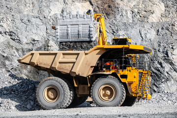 Large quarry excavator Loading gold ore into yellow dump truck for transportation to mining...