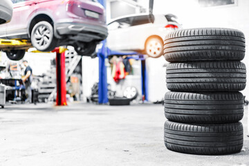 Stack of tires in a busy auto repair shop with cars on lifts in the background © Parilov