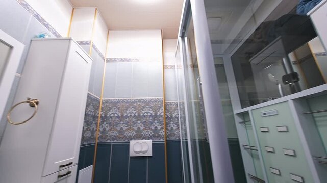 Modern bathroom with dark blue tiles, patterned accent wall, white sink, toilet, glass shower enclosure, mirrored cabinet, brass towel rings, sleek design.
