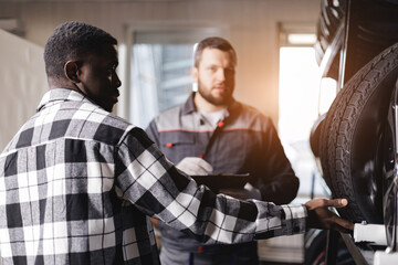 African young male discussing car repair with caucasian male mechanic in garage, sunlight