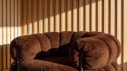 Modern brown velvet armchair in cozy minimalist interior with wooden slat wall and natural sunlight