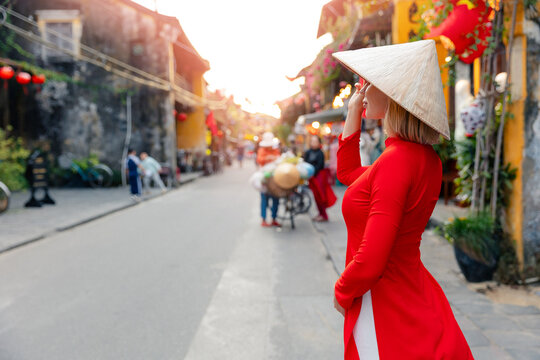Caucasian tourist female in red ao dai walking on hoi an street at sunset in vietnam