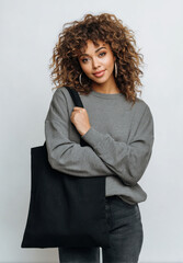 Young woman curly hair casual fashion grey sweatshirt black tote bag stylish model neutral background minimal style confident pose denim jean Young woman with curly hair grey sweatshirt and denim