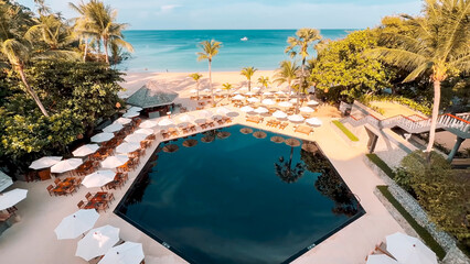 Fototapeta premium Aerial view of a hexagonal black pool surrounded by white umbrellas near the sea