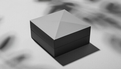 Minimalist black and white shot of a sleek gift box with a faceted lid, casting a sharp shadow on a textured surface, with soft light and shadow play in the background.