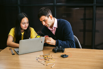 A young girl student and adult male teacher work together on a tech project with a laptop and electronics at a wooden table, highlighting STEM collaboration, innovation, and hands-on learning indoors.
